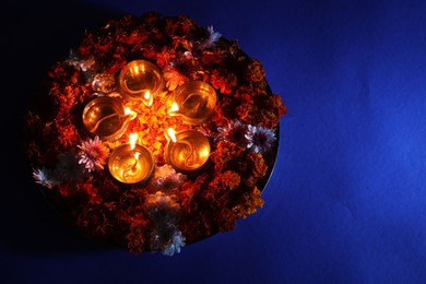 Photo of Diwali celebration. Diya lamps and beautiful flowers on blue background, top view. Space for text