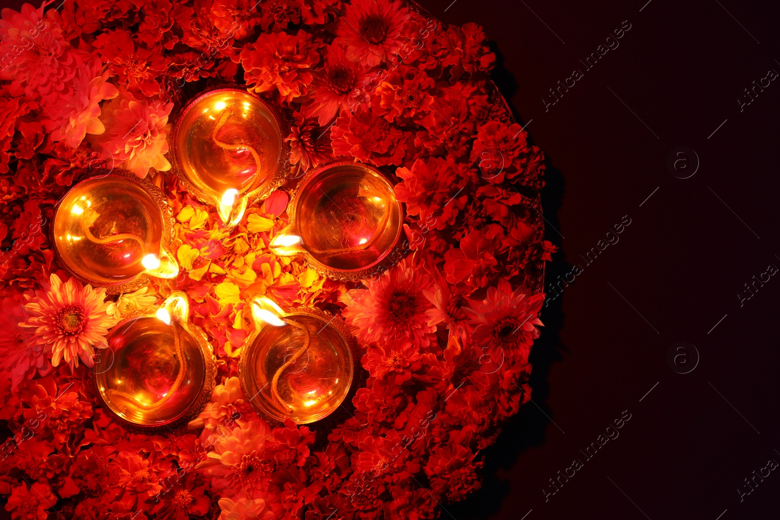 Photo of Diwali celebration. Diya lamps and beautiful flowers on dark background, top view. Space for text