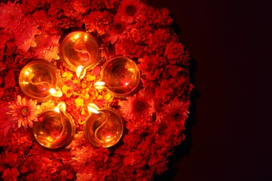 Photo of Diwali celebration. Diya lamps and beautiful flowers on dark background, top view. Space for text