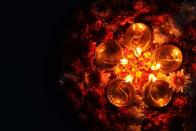 Photo of Diwali celebration. Diya lamps and beautiful flowers on dark background, top view. Space for text