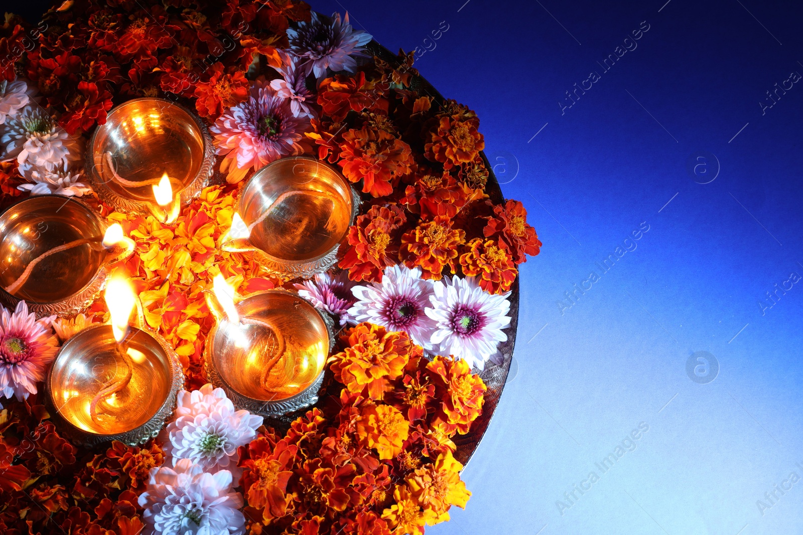 Photo of Diwali celebration. Diya lamps and beautiful flowers on blue background, top view. Space for text