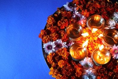 Photo of Diwali celebration. Diya lamps and beautiful flowers on blue background, top view. Space for text