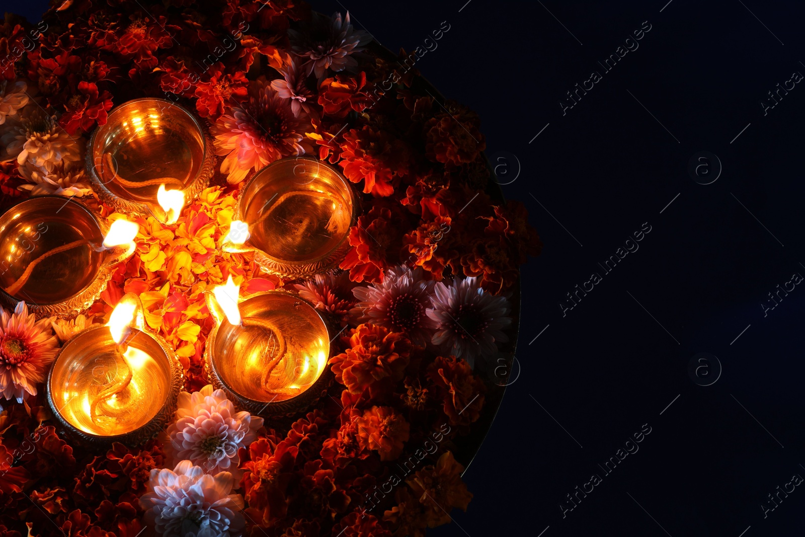 Photo of Diwali celebration. Diya lamps and beautiful flowers on dark background, top view. Space for text