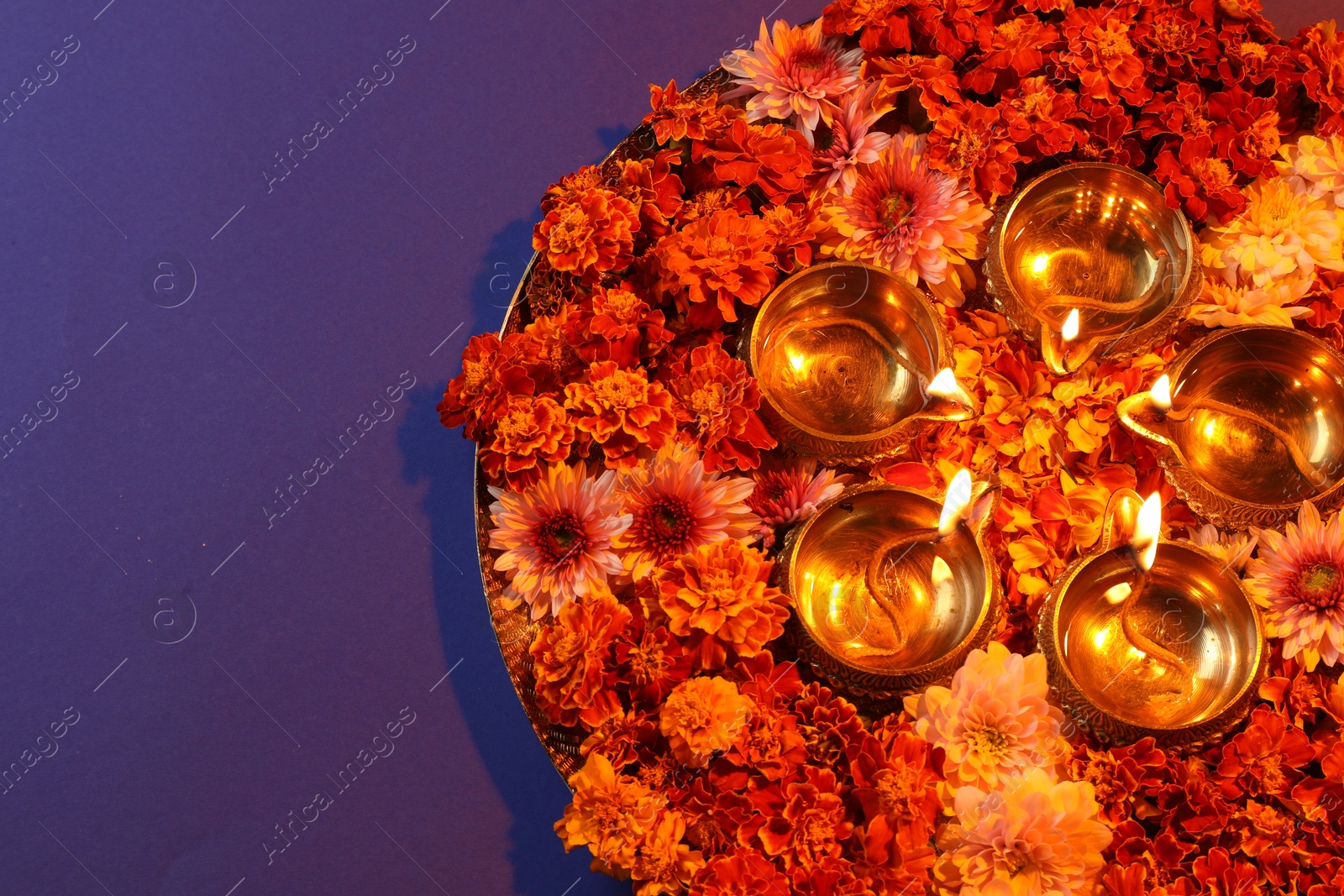 Photo of Diwali celebration. Diya lamps and beautiful flowers on violet background, top view. Space for text