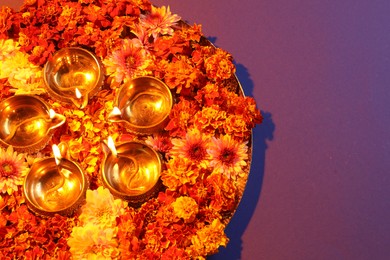 Photo of Diwali celebration. Diya lamps and beautiful flowers on violet background, top view. Space for text