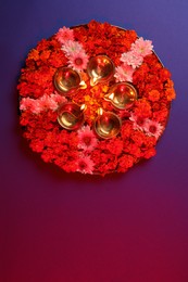 Photo of Diwali celebration. Diya lamps and beautiful flowers on color background, top view. Space for text