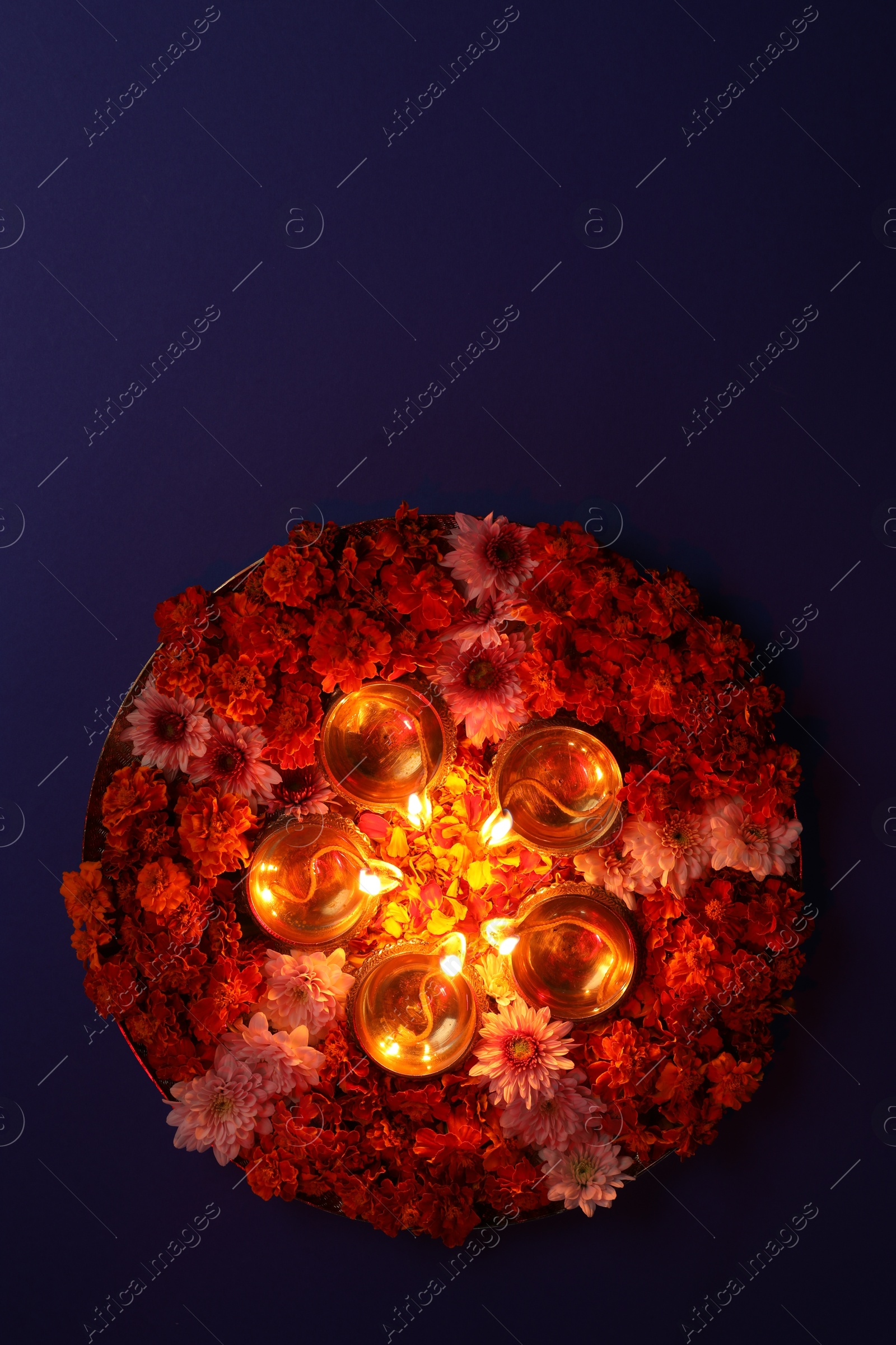 Photo of Diwali celebration. Diya lamps and beautiful flowers on violet background, top view. Space for text