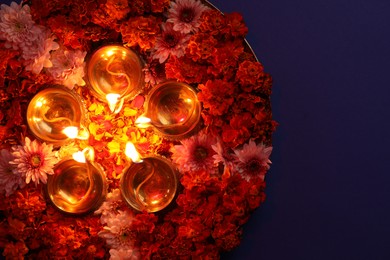 Photo of Diwali celebration. Diya lamps and beautiful flowers on violet background, top view