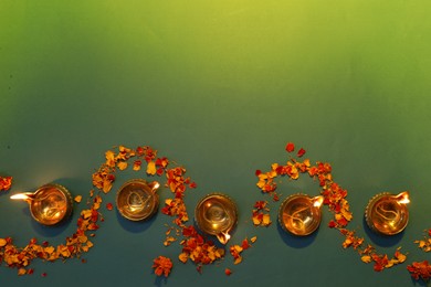 Photo of Diwali celebration. Diya lamps and beautiful flowers on green background, flat lay. Space for text