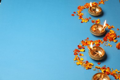 Diwali celebration. Diya lamps and marigold petals on light blue background, space for text