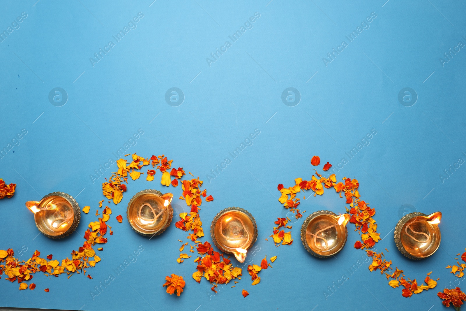 Photo of Diwali celebration. Diya lamps and marigold petals on light blue background, flat lay. Space for text