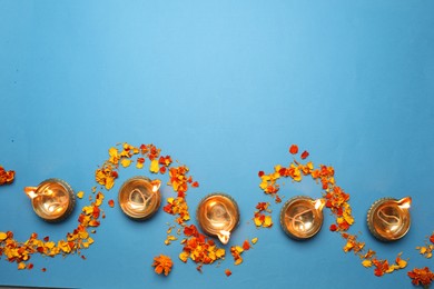 Photo of Diwali celebration. Diya lamps and marigold petals on light blue background, flat lay. Space for text