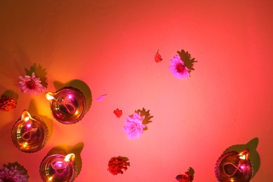 Diwali celebration. Diya lamps and beautiful flowers on red background, flat lay