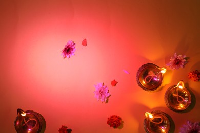 Photo of Diwali celebration. Diya lamps and beautiful flowers on red background, flat lay