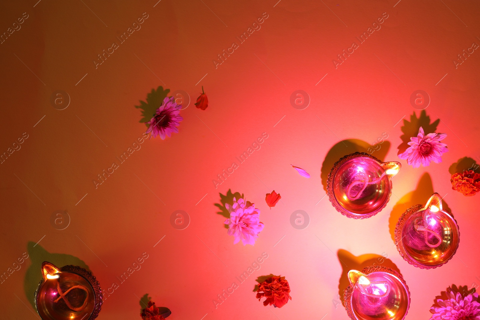 Photo of Diwali celebration. Diya lamps and beautiful flowers on red background, flat lay