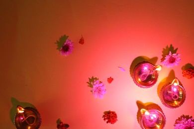 Photo of Diwali celebration. Diya lamps and beautiful flowers on red background, flat lay