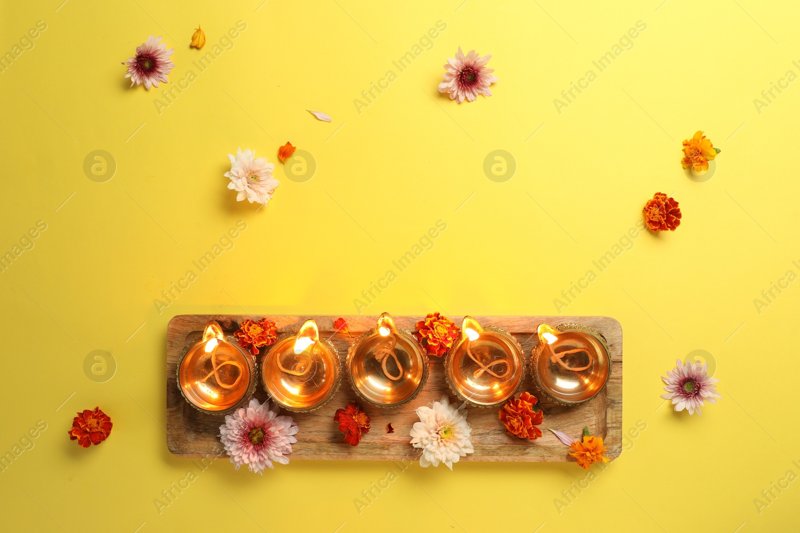 Photo of Diwali celebration. Diya lamps and beautiful flowers on yellow background, flat lay