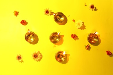 Photo of Diwali celebration. Diya lamps and beautiful flowers on yellow background, flat lay