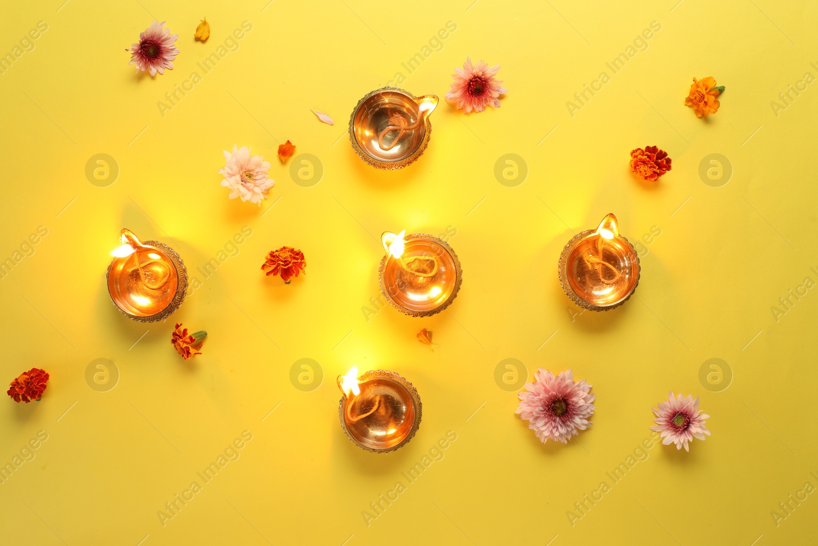 Photo of Diwali celebration. Diya lamps and beautiful flowers on yellow background, flat lay