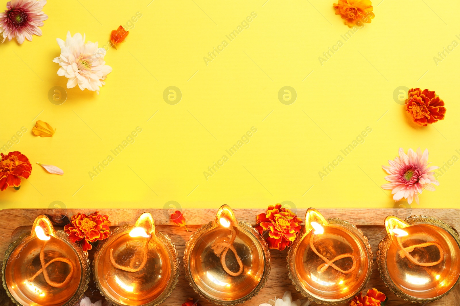 Photo of Diwali celebration. Diya lamps and beautiful flowers on yellow background, flat lay. Space for text