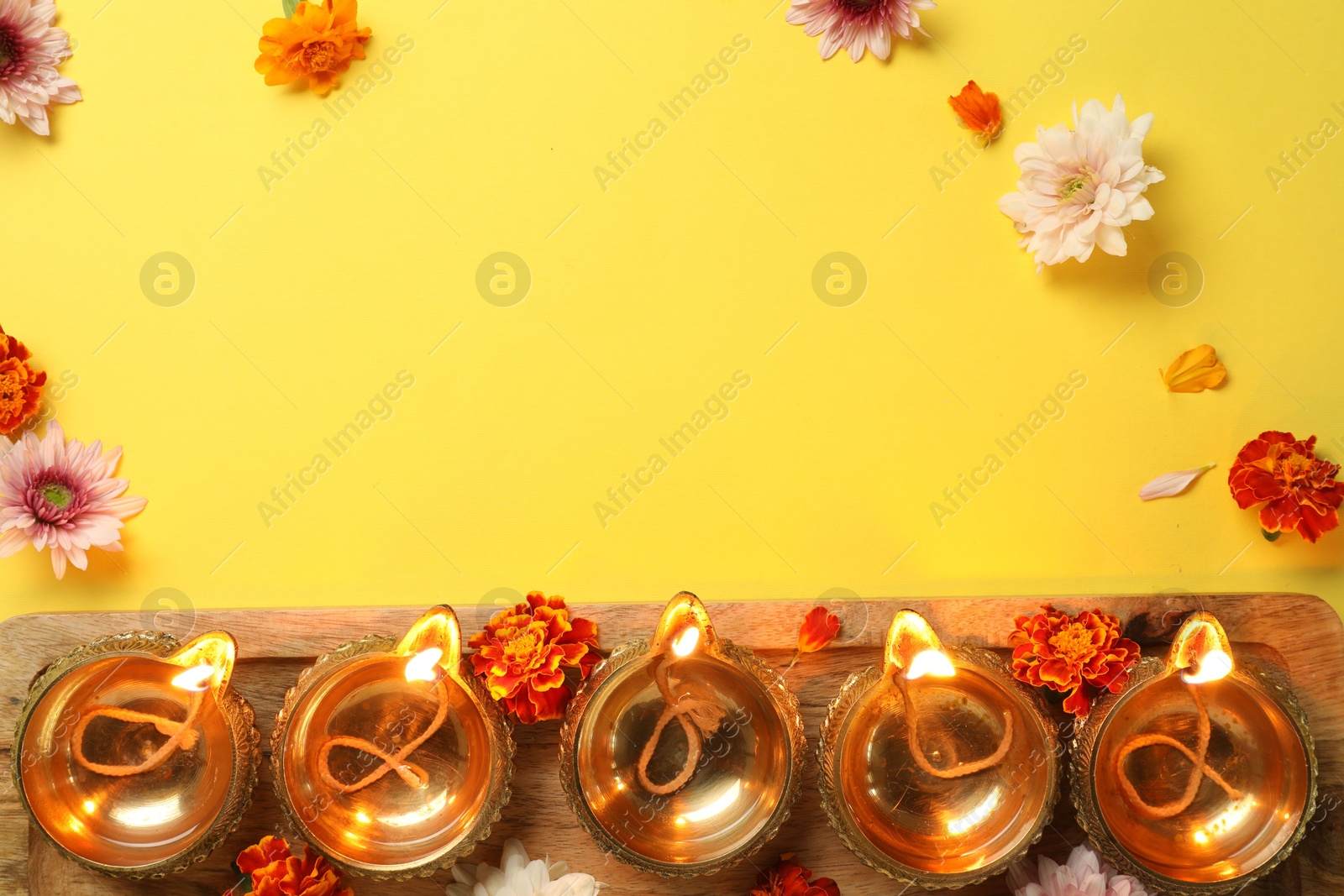 Photo of Diwali celebration. Diya lamps and beautiful flowers on yellow background, flat lay. Space for text