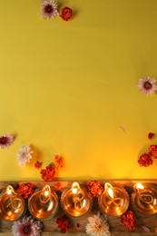 Diwali celebration. Diya lamps and beautiful flowers on yellow background, flat lay. Space for text