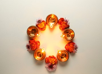 Photo of Diwali celebration. Diya lamps and beautiful flowers on light textured surface, flat lay. Space for text