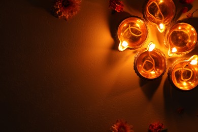 Diwali celebration. Diya lamps and beautiful flowers on dark textured surface, flat lay. Space for text