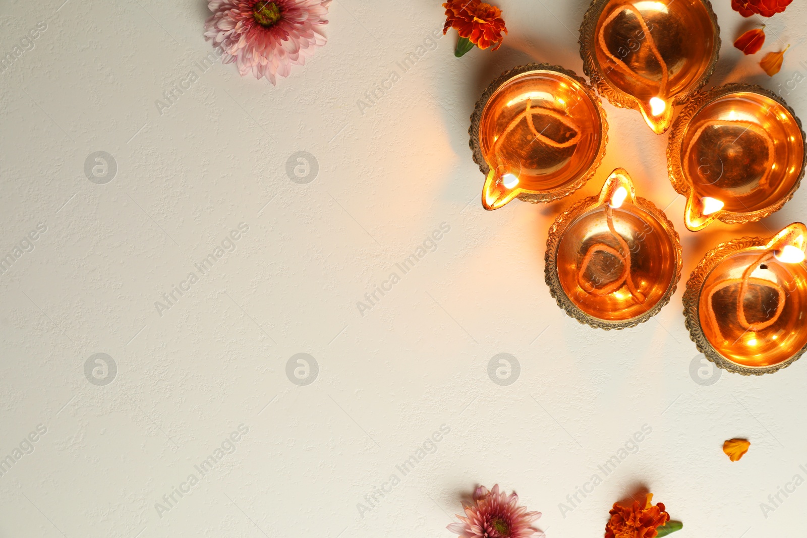 Photo of Diwali celebration. Diya lamps and beautiful flowers on light textured surface, flat lay. Space for text