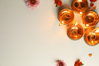 Photo of Diwali celebration. Diya lamps and beautiful flowers on light textured surface, flat lay. Space for text