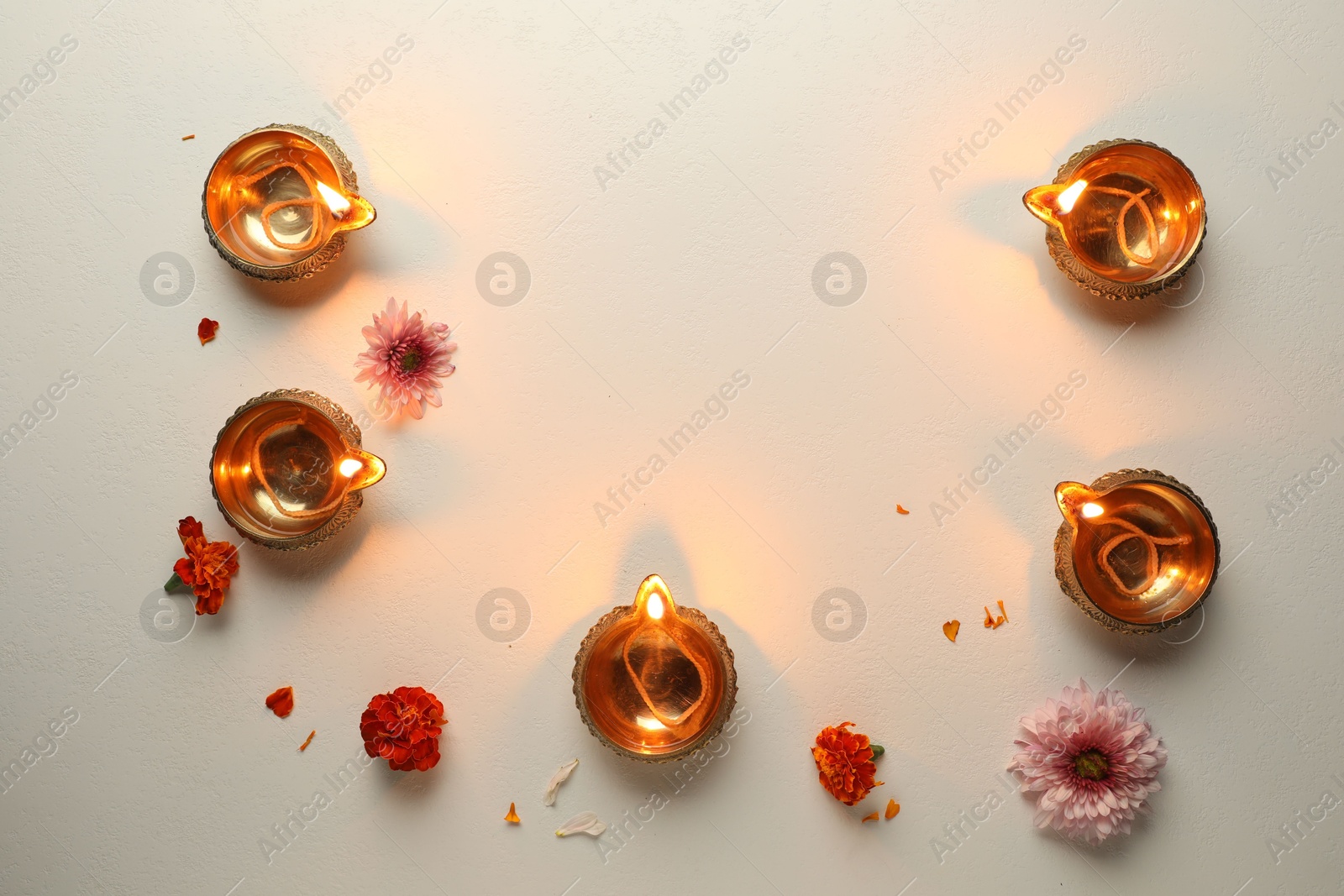 Photo of Diwali celebration. Diya lamps and beautiful flowers on light textured surface, flat lay. Space for text