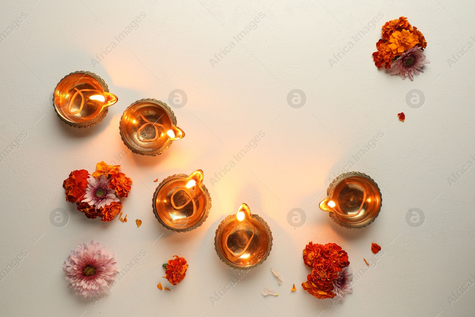 Photo of Diwali celebration. Diya lamps and beautiful flowers on light textured surface, flat lay. Space for text