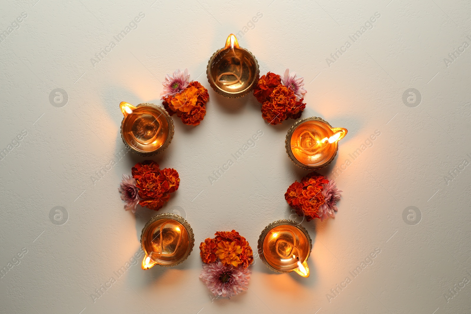 Photo of Diwali celebration. Diya lamps and beautiful flowers on light textured surface, flat lay. Space for text