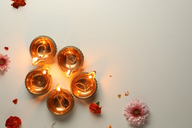 Photo of Diwali celebration. Diya lamps and beautiful flowers on light textured surface, flat lay. Space for text