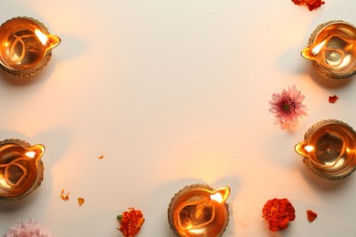 Photo of Diwali celebration. Diya lamps and beautiful flowers on light textured surface, flat lay. Space for text