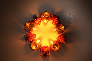 Diwali celebration. Diya lamps and beautiful flowers on dark textured surface, flat lay. Space for text