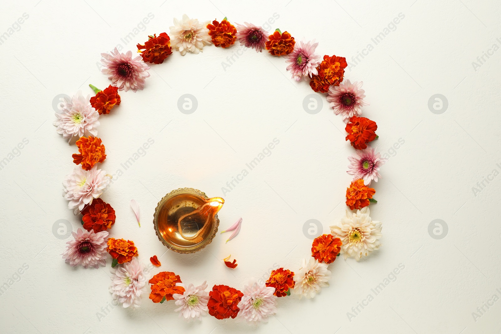 Photo of Diwali celebration. Diya lamp and beautiful flowers on light textured surface, flat lay. Space for text