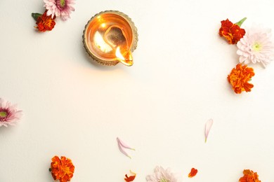 Photo of Diwali celebration. Diya lamp and beautiful flowers on light textured surface, flat lay. Space for text