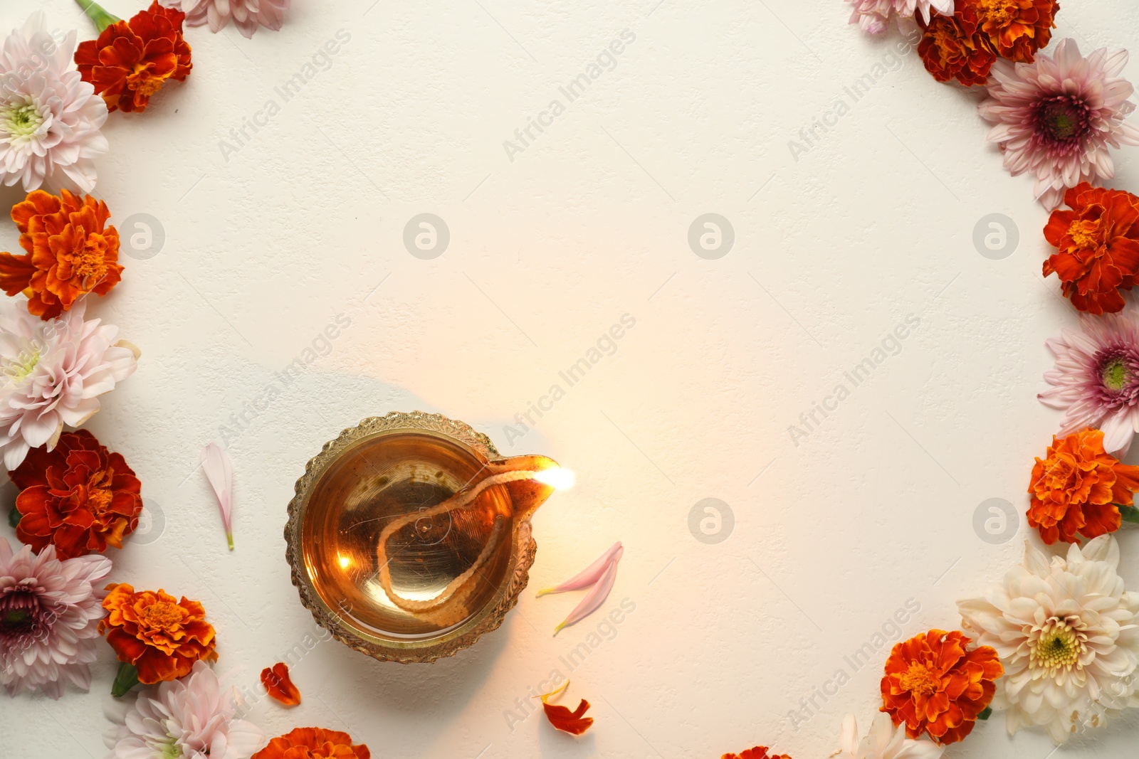 Photo of Diwali celebration. Diya lamp and beautiful flowers on light textured surface, flat lay. Space for text