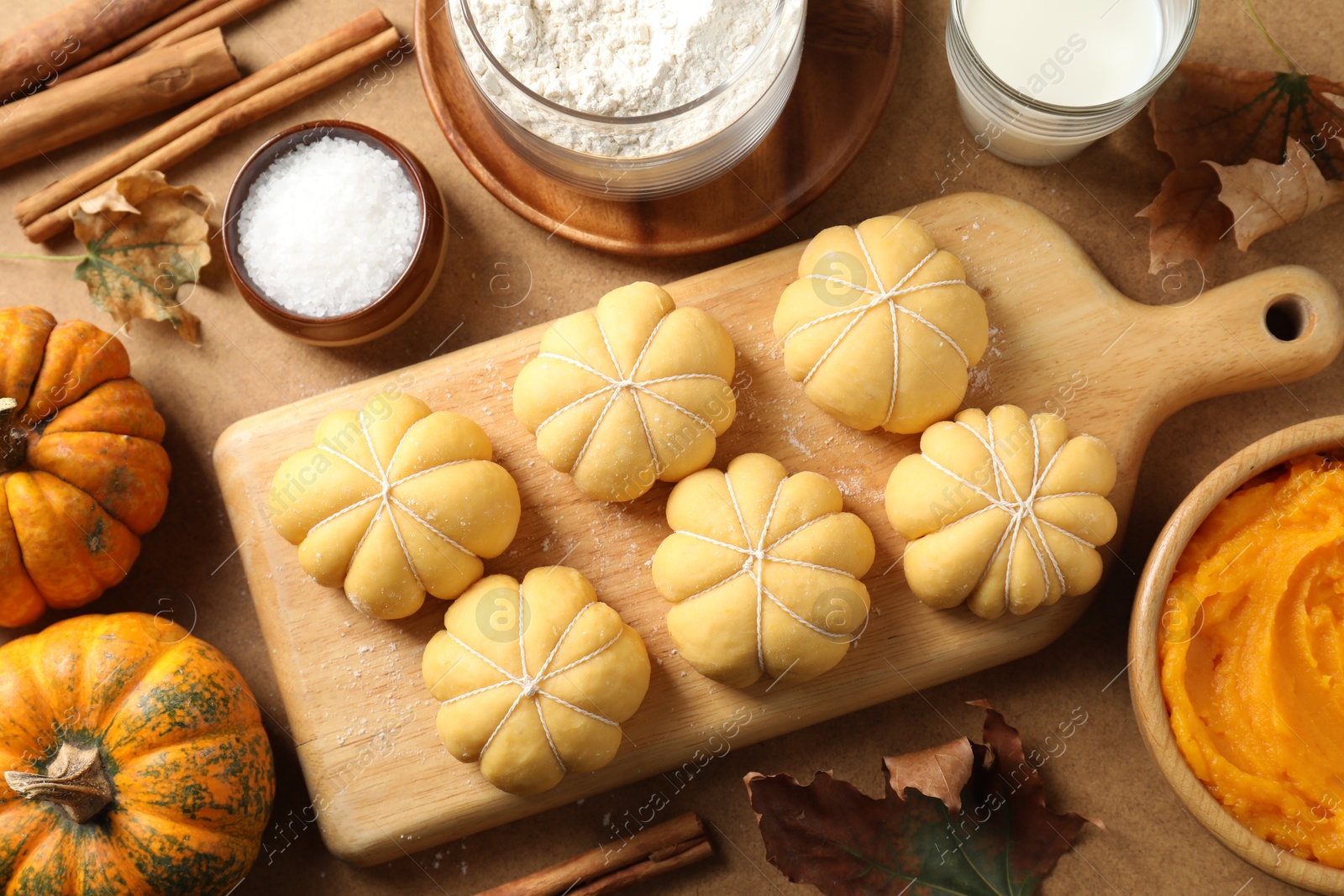 Photo of Raw pumpkin shaped buns and ingredients on brown table, flat lay