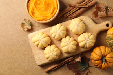 Photo of Raw pumpkin shaped buns and ingredients on brown table, flat lay