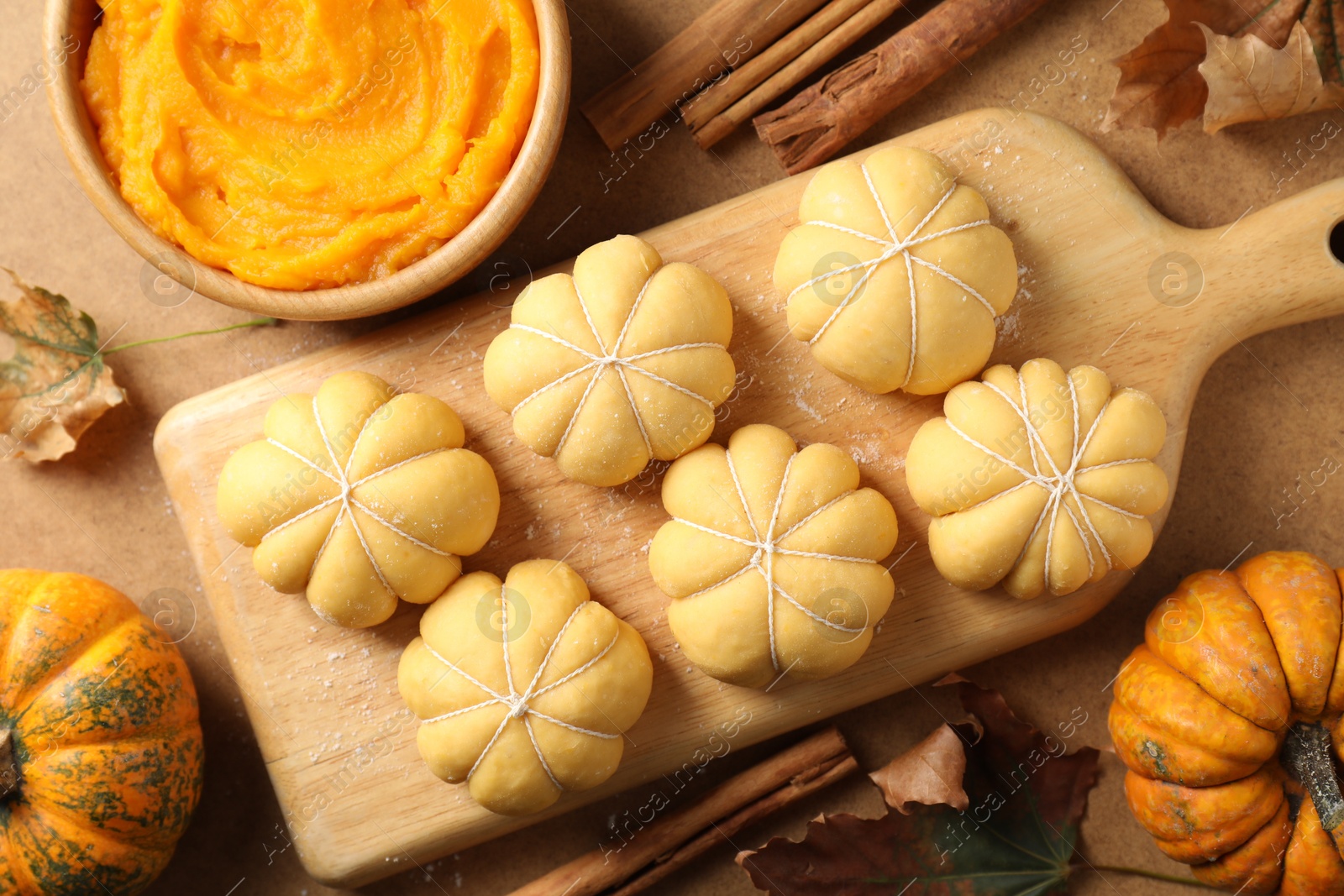 Photo of Raw pumpkin shaped buns and ingredients on brown table, flat lay