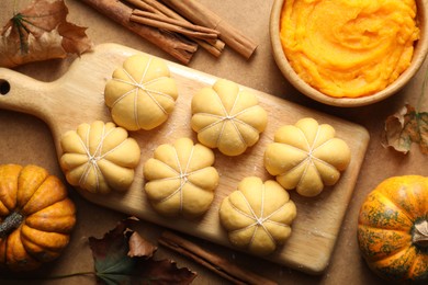 Photo of Raw pumpkin shaped buns and ingredients on brown table, flat lay