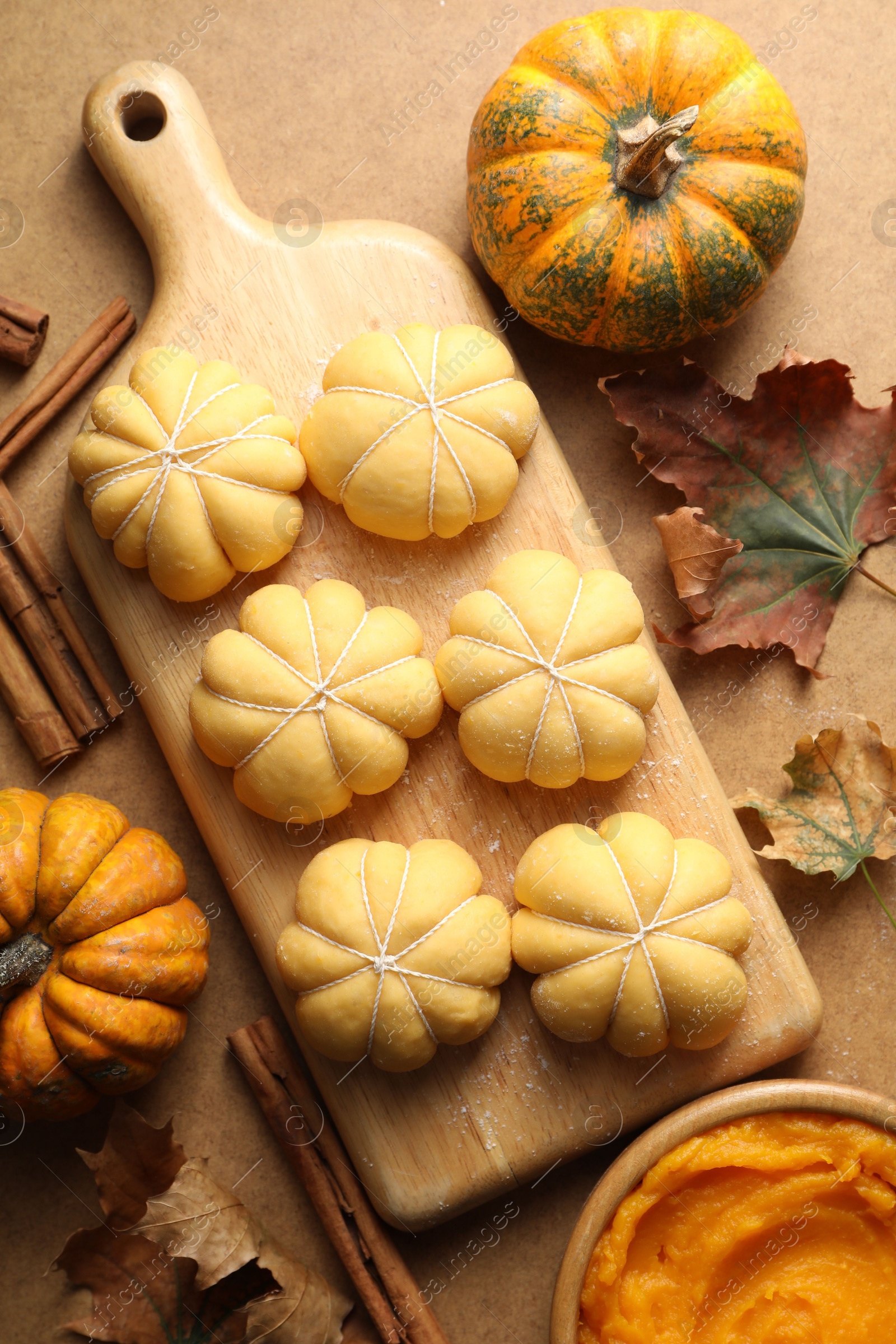 Photo of Raw pumpkin shaped buns and ingredients on brown table, flat lay