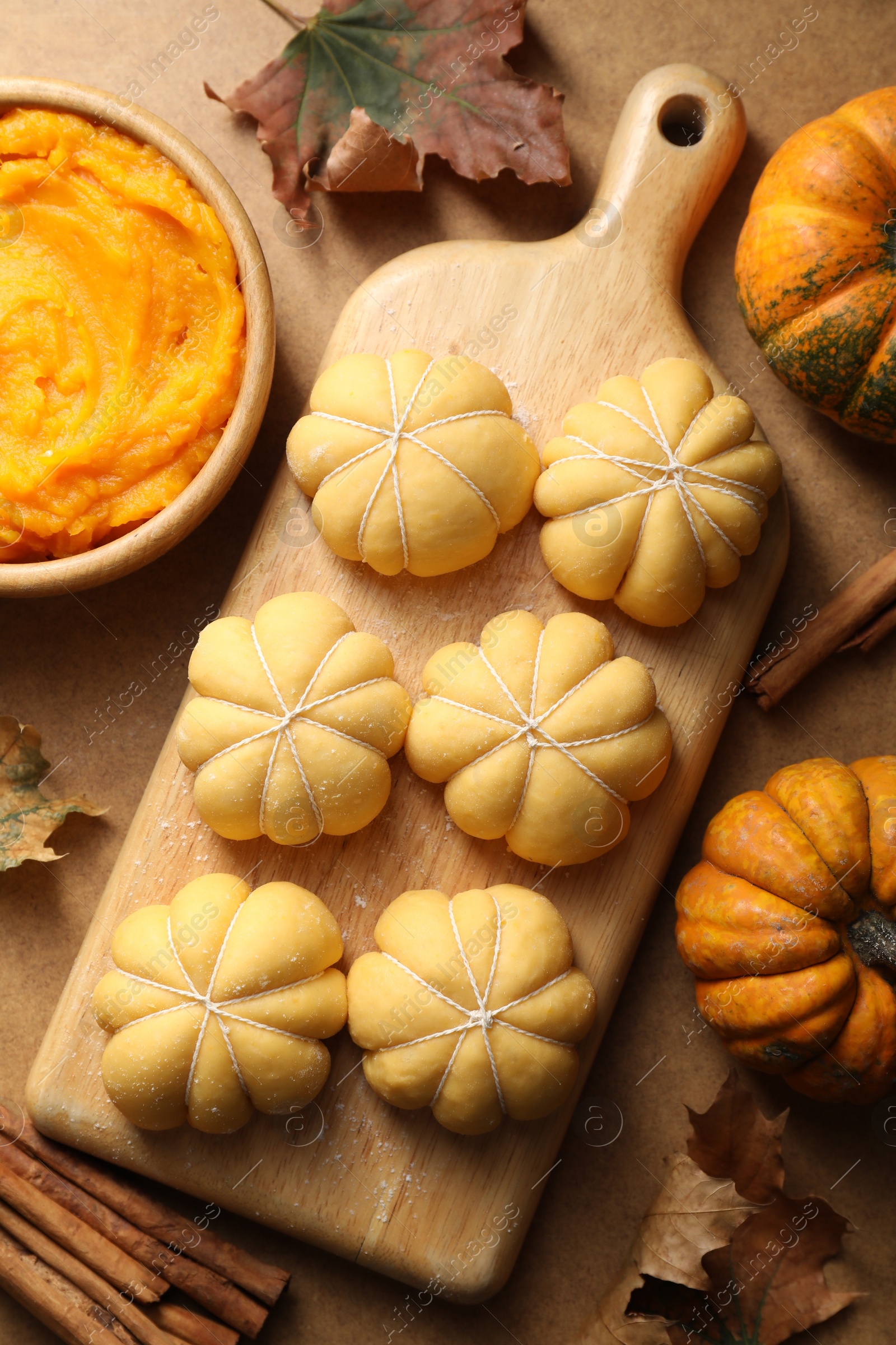 Photo of Raw pumpkin shaped buns and ingredients on brown table, flat lay