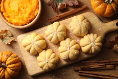 Photo of Raw pumpkin shaped buns and ingredients on brown table, flat lay