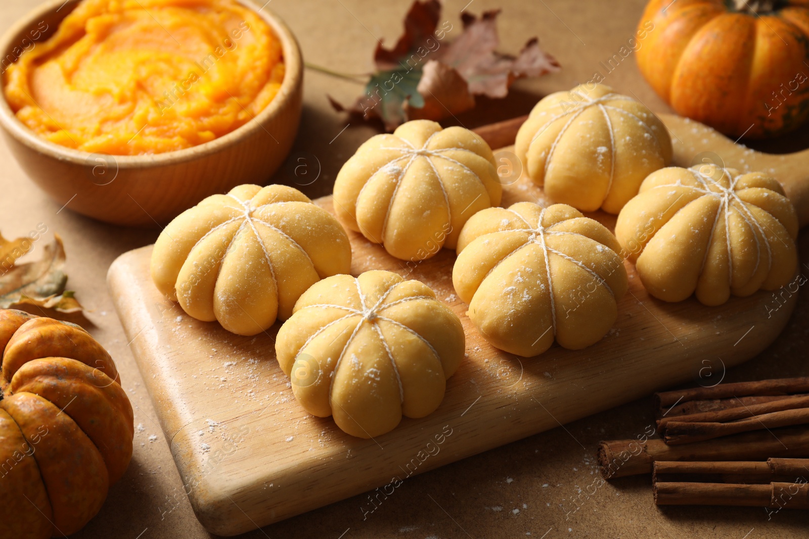 Photo of Raw pumpkin shaped buns and ingredients on brown table