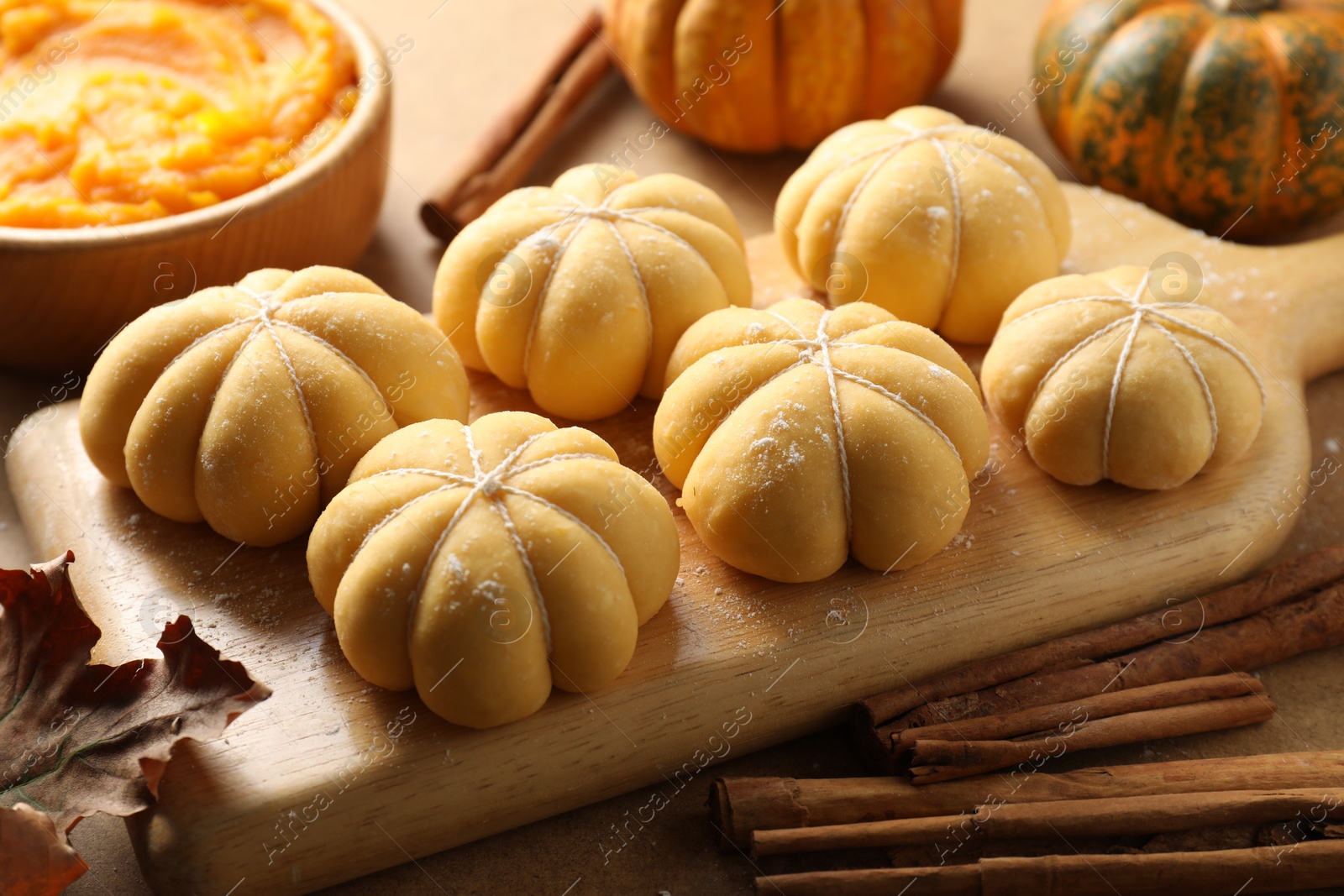 Photo of Raw pumpkin shaped buns and ingredients on brown table, closeup