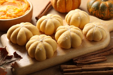 Photo of Raw pumpkin shaped buns and ingredients on brown table, closeup