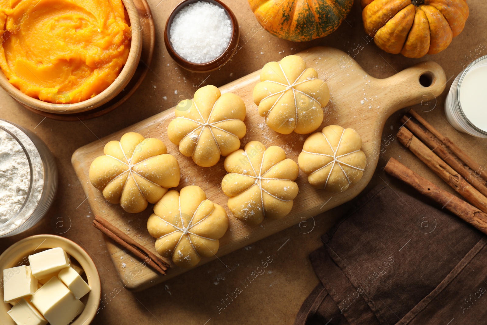 Photo of Raw pumpkin shaped buns and ingredients on brown table, flat lay